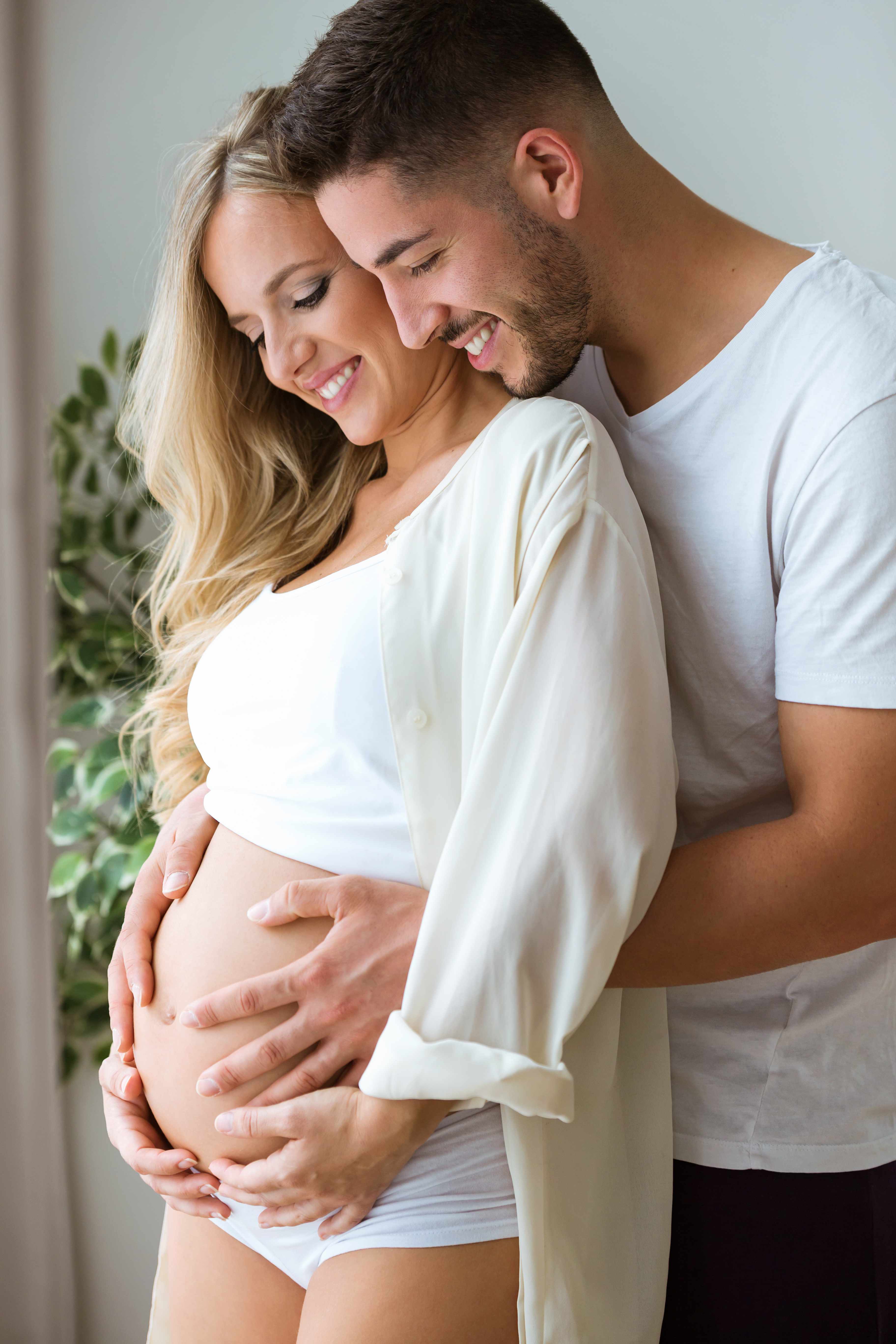 Handsome young man touching and looking belly of beautiful pregnant woman at home.