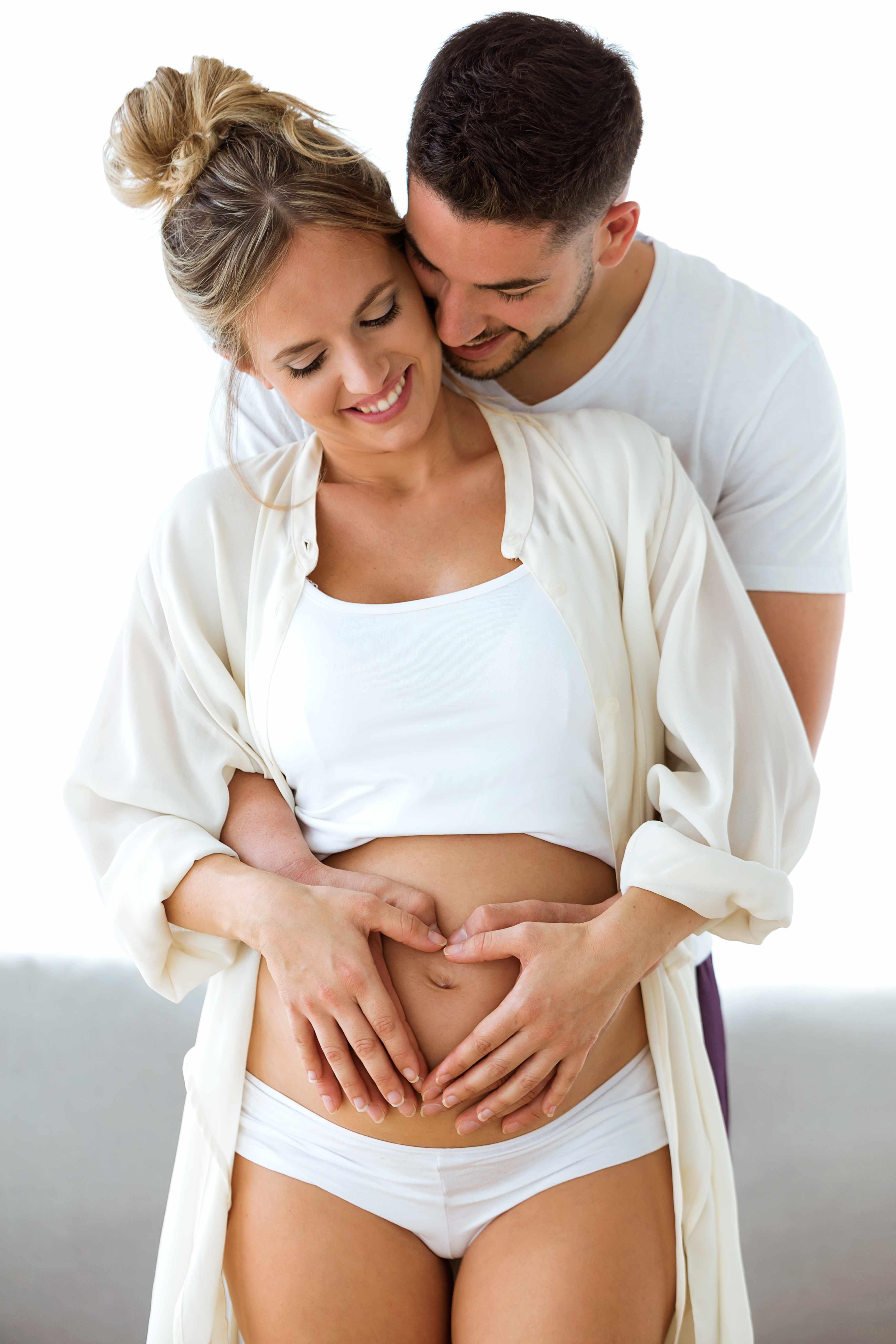 Handsome young man holding belly of his pregnant wife making heart together at home.